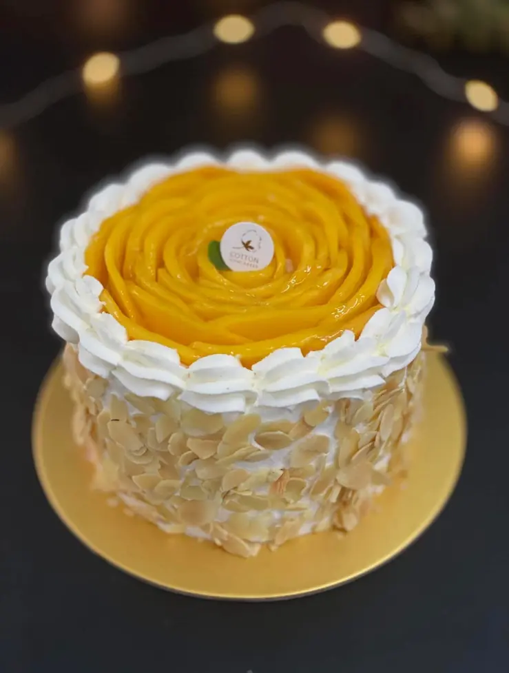 Small mango rose cake on a gold board with fairy lights behind