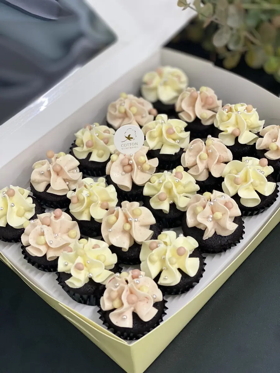 Box of chocolate cupcakes with piped pastel cream and pearl sprinkles